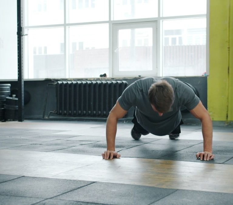 Young man is doing push-ups exercising in gym with female coach enjoying exercise indoors. Active millennials, sports and modern lifestyle concept.